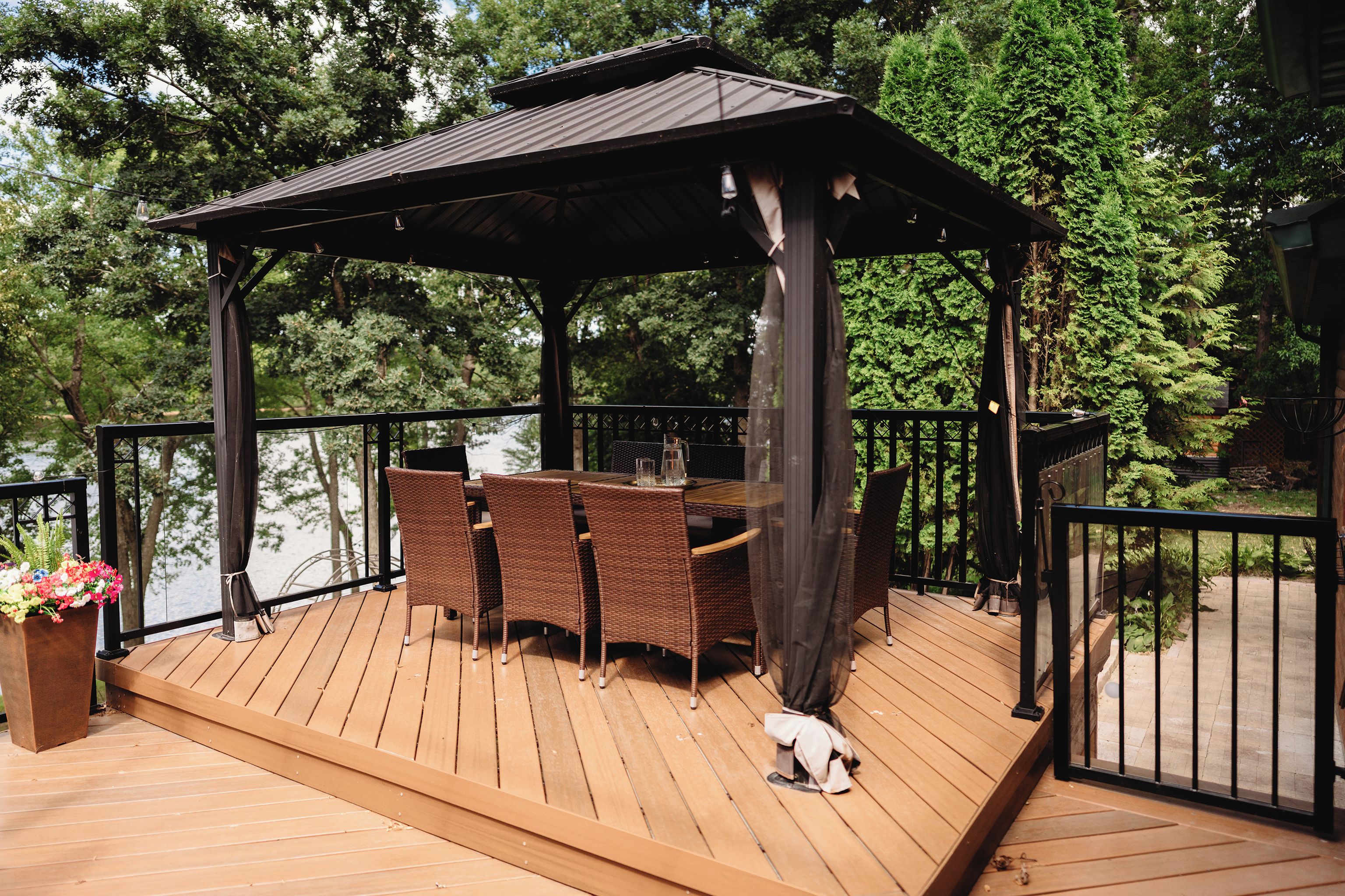 A wooden deck with a gazebo, wicker furniture, and a small dog.