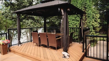 A wooden deck with a gazebo, wicker furniture, and a small dog.