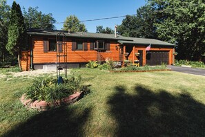 Eine Blockhütte mit Garage, umgeben von einer gepflegten Rasenfläche und verschiedenen Pflanzen.