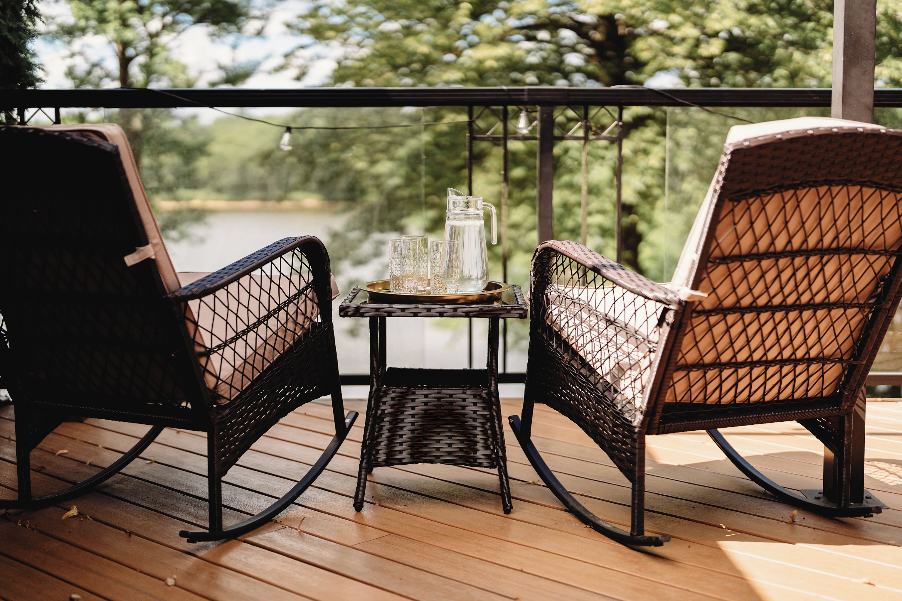 A wooden deck with two wicker rocking chairs and a small table with a pitcher and glasses.
