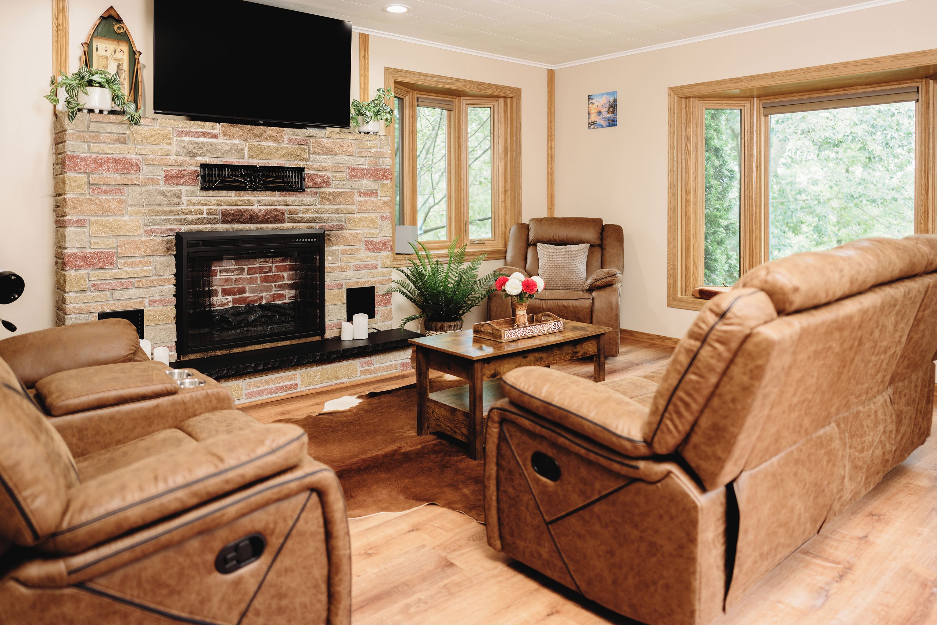 A living room with a fireplace, leather sofas, a television, and large windows.