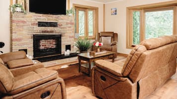A living room with a fireplace, leather sofas, a television, and large windows.