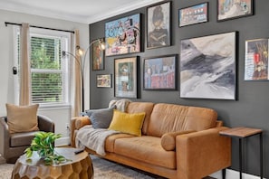 A living room with a brown leather sofa, a round wooden coffee table, and a floor lamp. - Charlotte Escape | Near NoDa & Plaza Midwood (Charlotte)