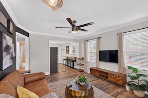 A modern living room with a sofa, coffee table, TV, and a ceiling fan. - Belmont Duplex | Shops, Dining & Entertainment (Charlotte)