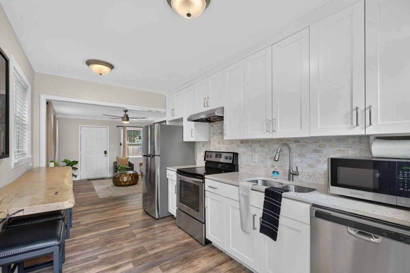 A modern kitchen with white cabinets, stainless steel appliances, and a wooden floor.