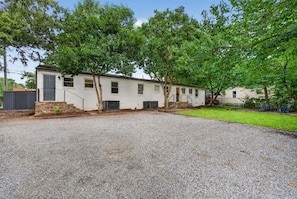 A residential property with a gravel driveway, a white building with a grey door, and a green lawn. - Belmont Duplex | Shops, Dining & Entertainment (Charlotte)