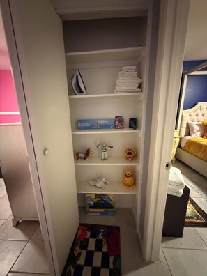 A narrow hallway with a door leading to a room. The hallway has a checkered rug on the floor and a shelf with various items including a toy, a book, and a box. - Charming 2-bedroom apartment with AC in lively Phoenix (Phoenix)