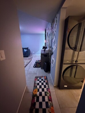 A hallway with a checkered mat leading to a room with a washing machine. - Charming 2-bedroom apartment with AC in lively Phoenix (Phoenix)