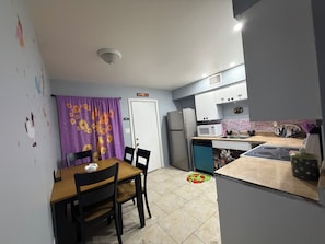 A compact kitchen with a refrigerator, microwave, and stove. There is a dining table with chairs and a purple curtain. - Charming 2-bedroom apartment with AC in lively Phoenix (Phoenix)