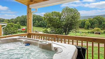 A hot tub on a wooden deck with a view of a green landscape and trees.