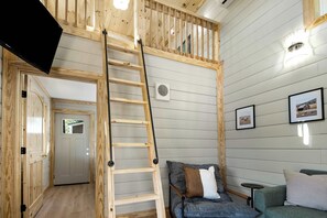 A room with a wooden ladder, a grey sofa, and a small table. - Green Getaway Cabin with Pasture Views (Chattanooga)