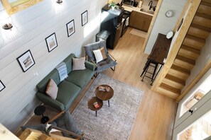 Een moderne leefruimte met een groene bank, een salontafel en een keuken met een magnetron en spoelbak.