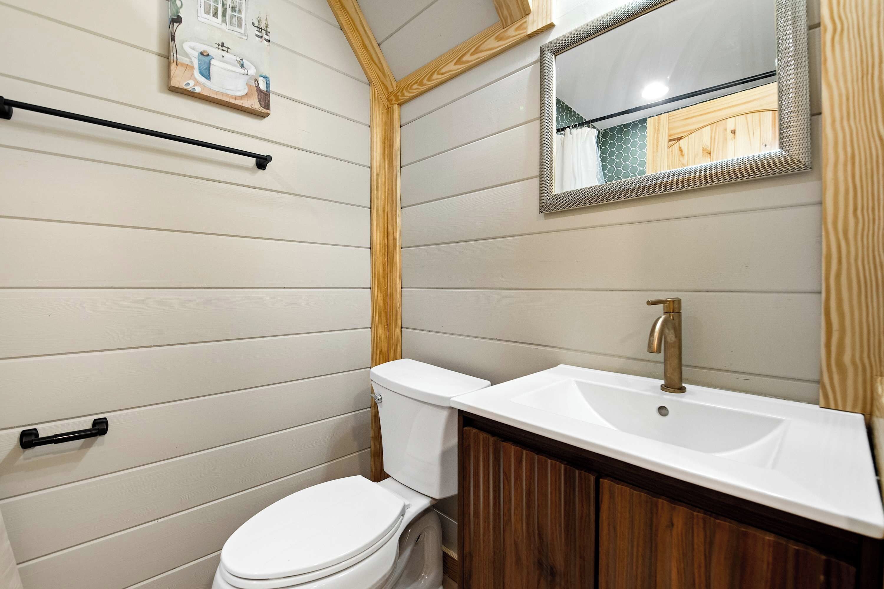 A bathroom with a white toilet, wooden vanity, and a mirror with a wooden frame.