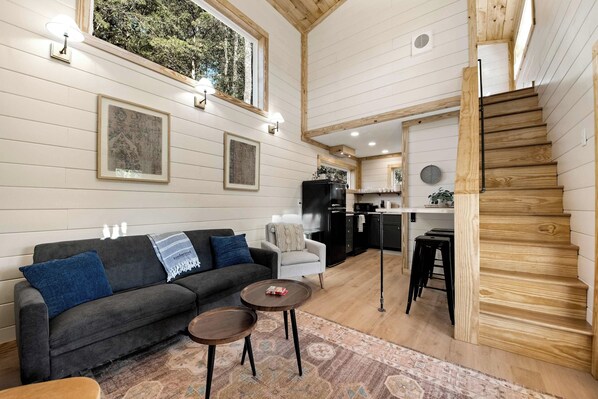 Een modern interieur met een grijze bank, twee kleine tafels, een trap en een keukenhoek.