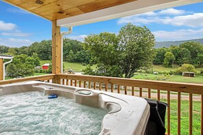 Een hottub op een houten terras met uitzicht op een groen landschap en bomen.