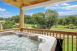 Een hottub op een houten terras met uitzicht op een groen landschap en bomen.