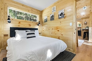 Een slaapkamer in een houten hutje, met een bed, een raam en foto's aan de muur.