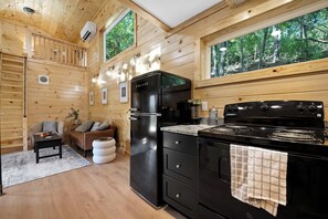 A modern kitchen with a black stove, a refrigerator, and a coffee maker. There are wooden walls and a window with a view of trees. - 3 Cabin Rental on Private Farm, 15 mins from Chatt (Chattanooga)