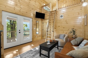 Interior em madeira com TV, escada, sofá e mesa de centro.