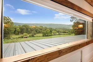 A view from a window with a metal roof, overlooking a green landscape with trees and a hill in the distance. - 3 Cabin Rental on Private Farm, 15 mins from Chatt (Chattanooga)