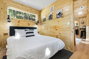 A wooden cabin bedroom with a bed, a window, and wall-mounted pictures. - 3 Cabin Rental on Private Farm, 15 mins from Chatt (Chattanooga)