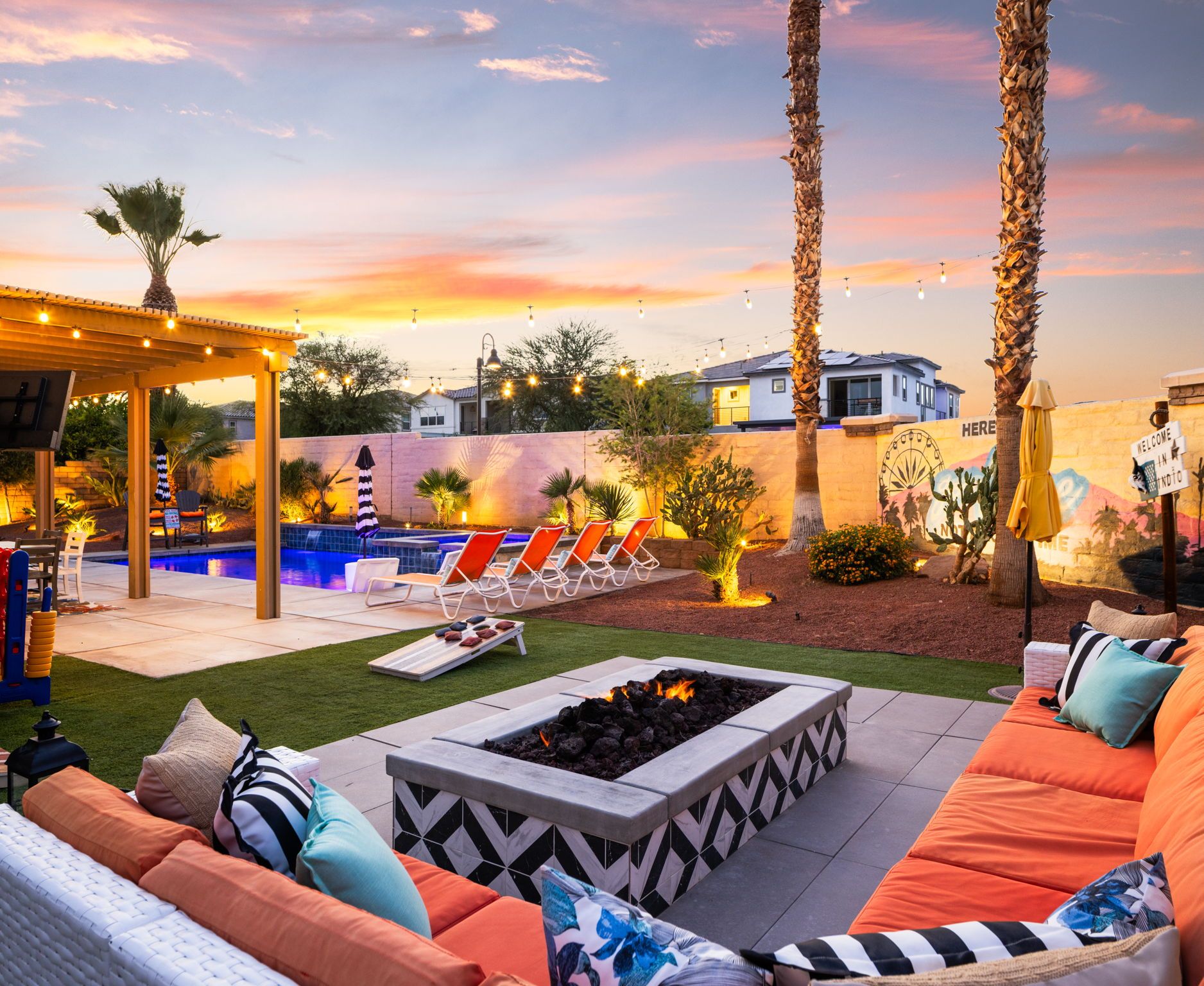A backyard with a pool, lounge chairs, a fire pit, and a pergola.