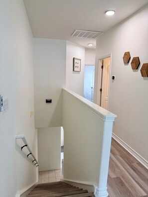 A staircase with a white handrail and wooden steps leading to a landing. - Full Renovated Coastal Retreat, Walk to Beach, Modern, Pool, Patio, Balcony. (Corpus Christi)