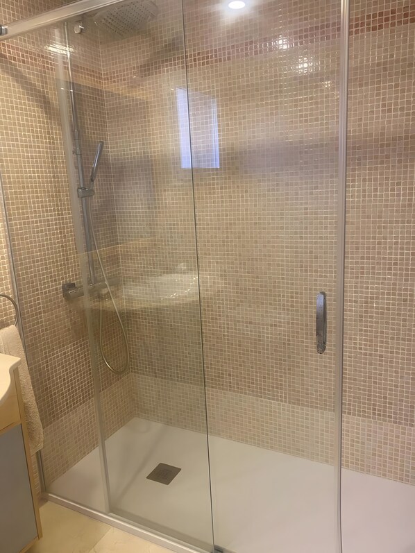 A glass-enclosed shower with a tiled wall, a control panel, and a handheld showerhead.