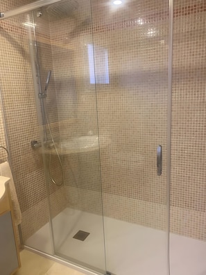 A glass-enclosed shower with a tiled wall, a control panel, and a handheld showerhead. - Apartment 'Duplex En Estepona' with Shared Pool, Wi-Fi and Air Conditioning (Estepona)