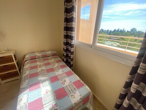 Une petite chambre avec un lit simple et une fenêtre donnant sur un paysage verdoyant.