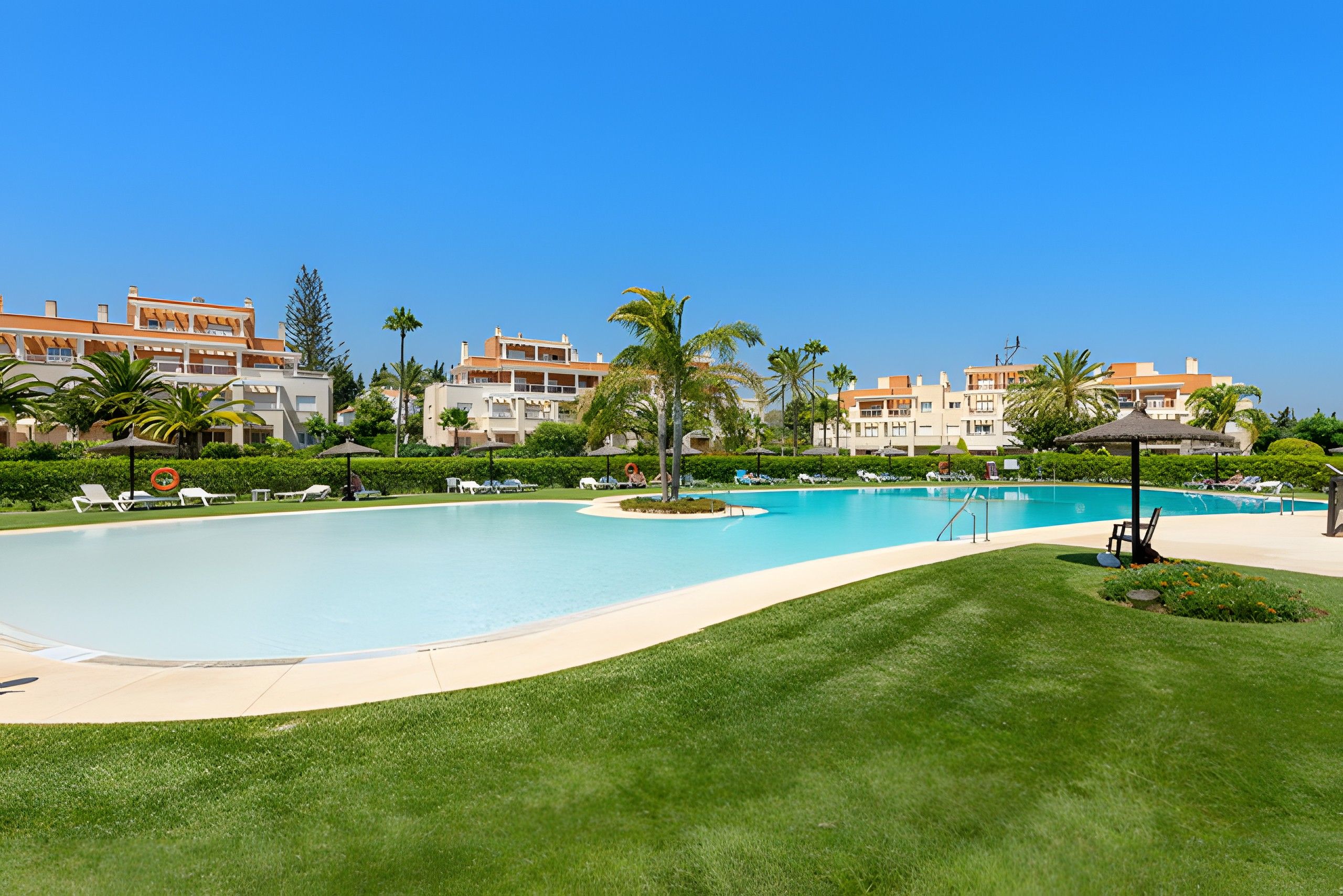 A resort with a large swimming pool, palm trees, and a well-maintained lawn.