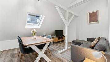 Ein stilvoller Wohnraum mit Esstisch, Stühlen, einer Couch, einem Fernseher und einem kleinen Fenster.