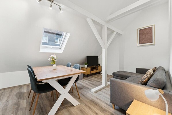 Ein stilvoller Wohnraum mit Esstisch, Stühlen, einer Couch, einem Fernseher und einem kleinen Fenster.