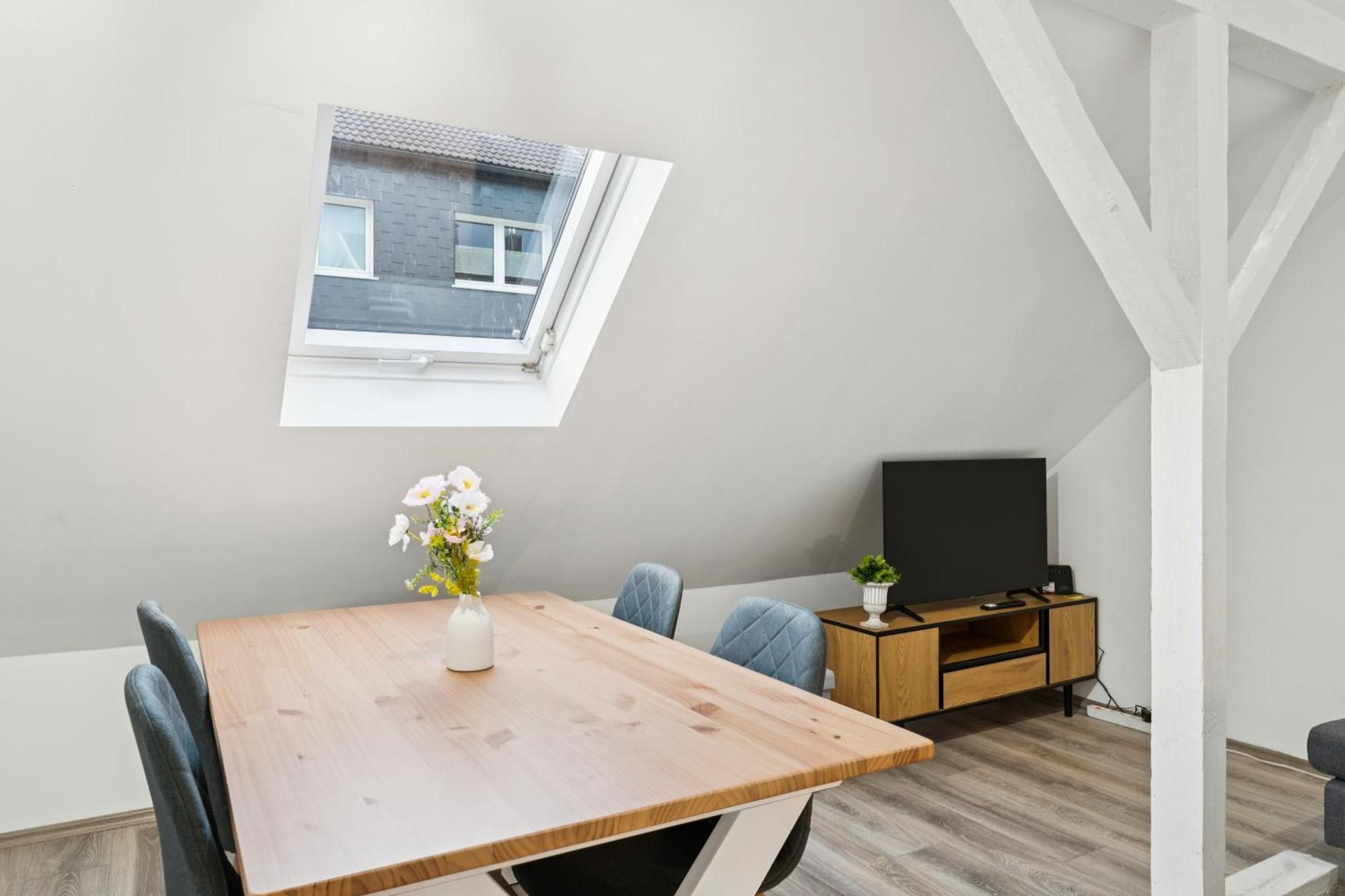 Ein modernes, kompaktes Wohnzimmer mit Dachfenster, einem Esstisch, einem Fernseher und einer kleinen Kommode.