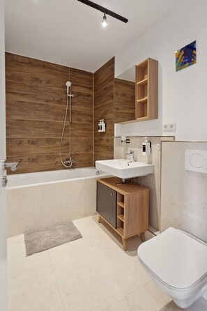 Ein modernes Badezimmer mit einer Holzwand, einer Badewanne, einem Waschbecken und einer Toilette.