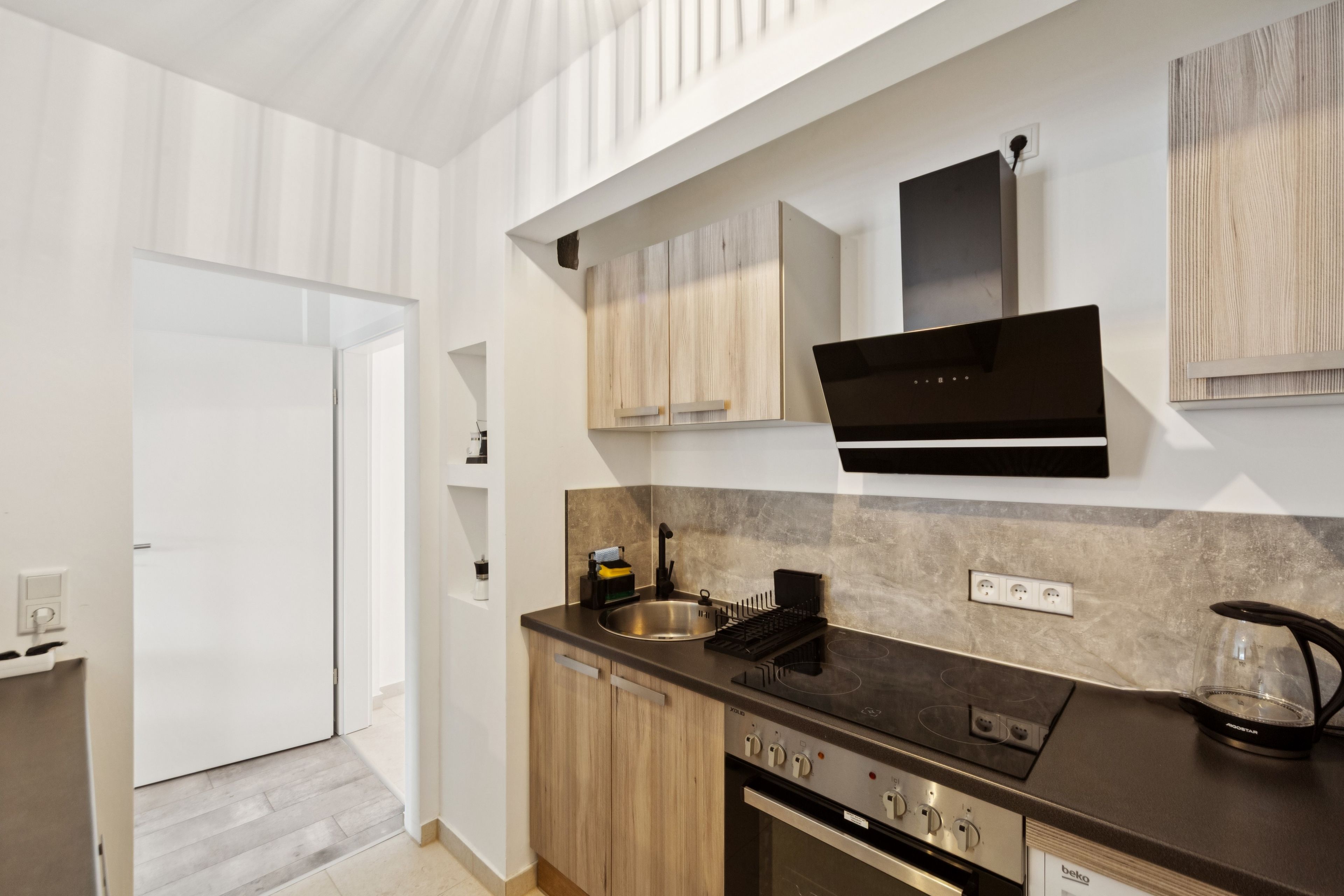 Una cocina moderna con estufa, horno y pileta integrados. Hay un armario de madera sobre la estufa y un extractor de aire negro.