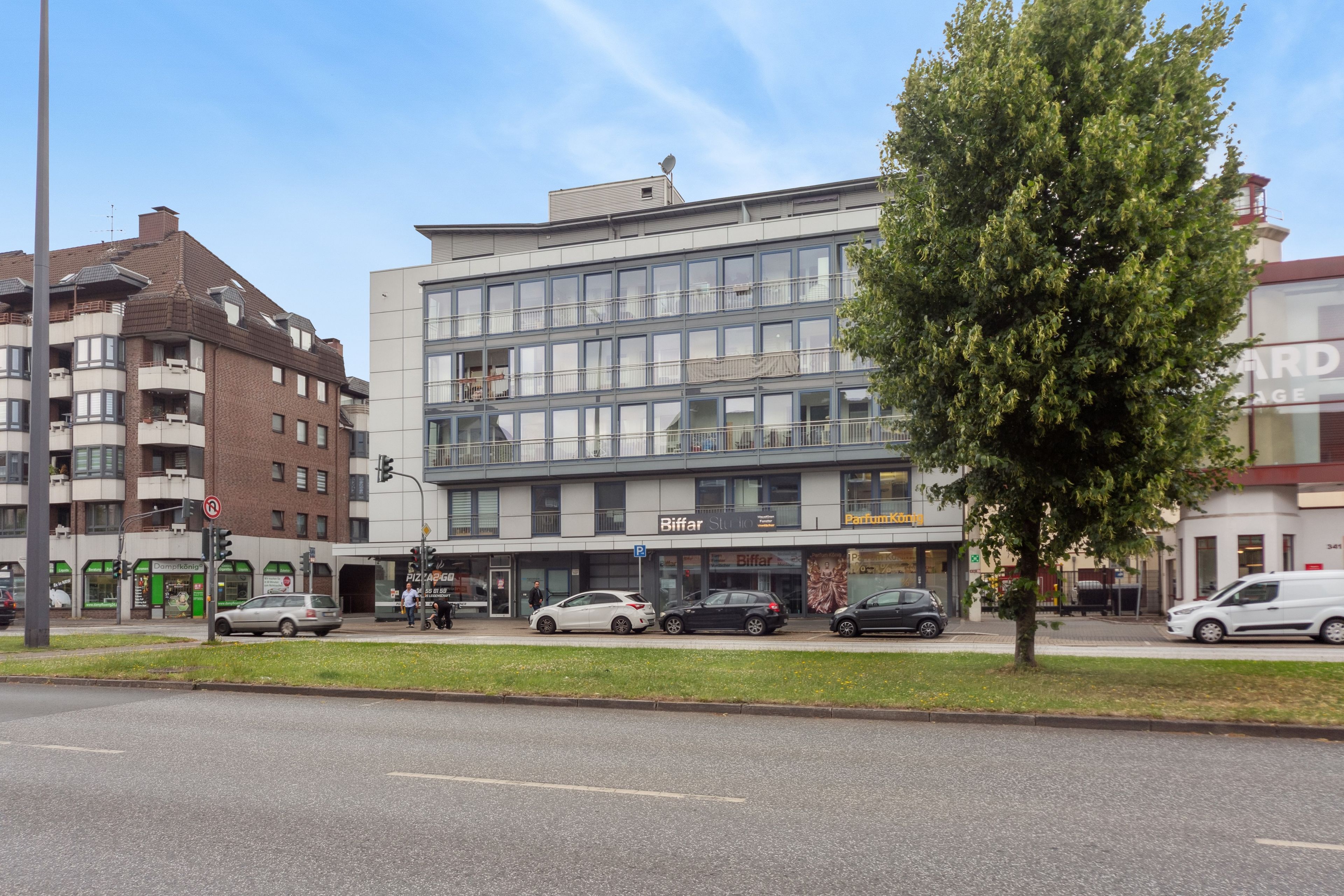 Ein mehrgeschossiges Gebäude mit moderner Fassade, mit einem Ladenlokal im Erdgeschoss, auf dem die Schilder 'Biffar Studio' und 'ParfumKönig' sichtbar sind.