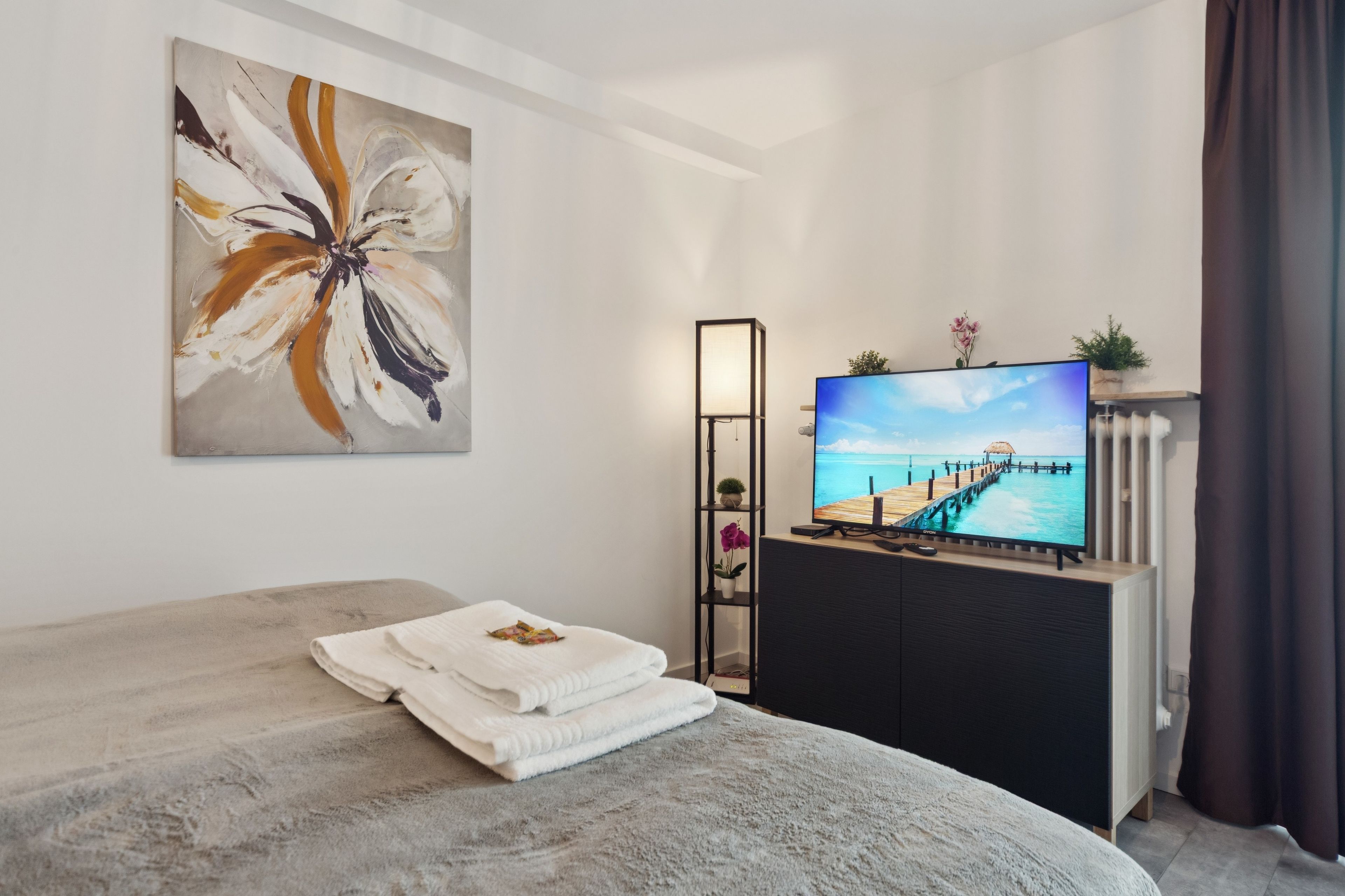 Ein Hotelzimmer mit einem Bett, einem an einem Standfuß befestigten Flachbildfernseher, einem Gemälde an der Wand und Blick auf einen Steg.
