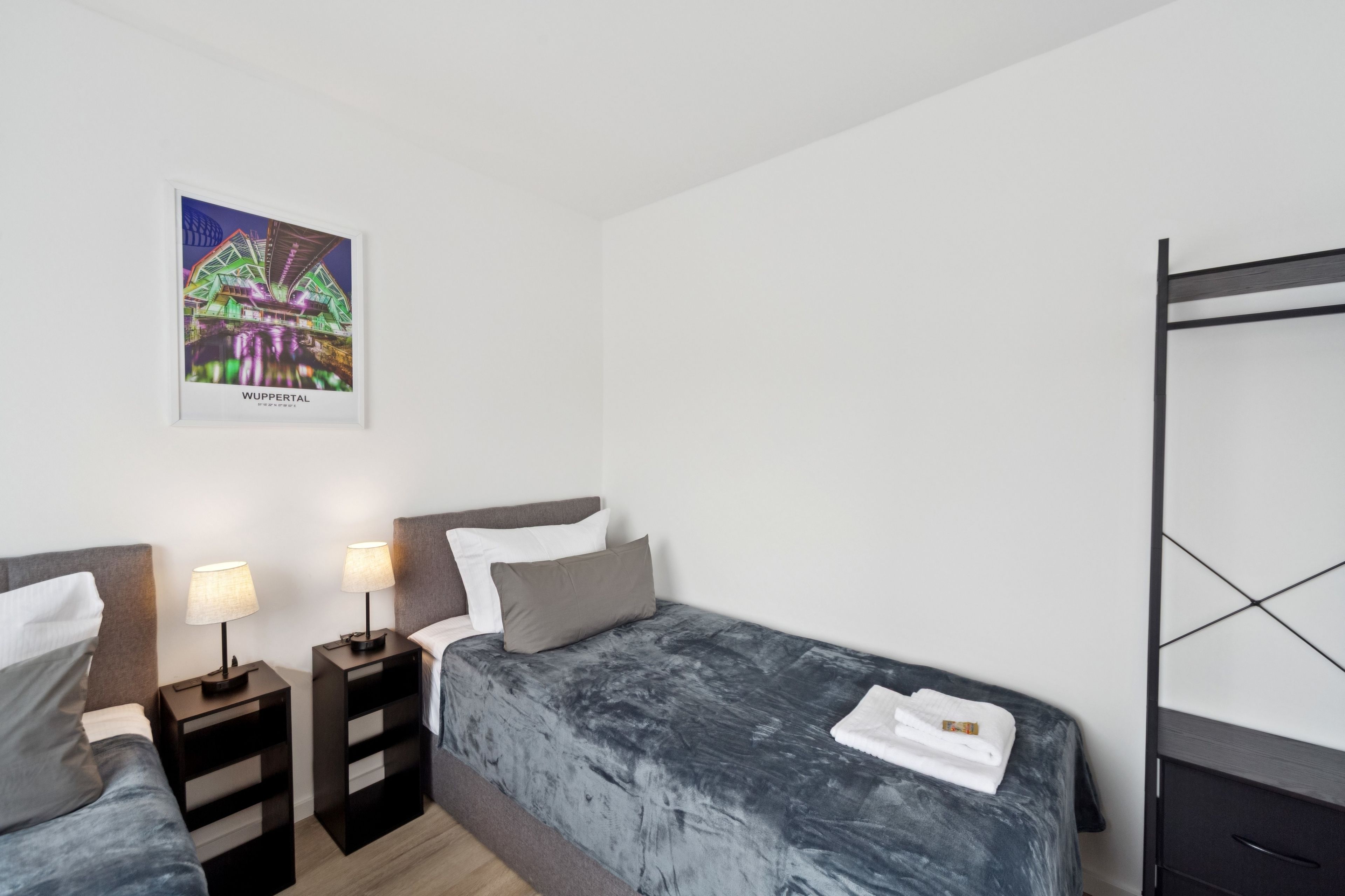 Habitación de hotel con dos camas, una litera, un cuadro de un edificio y una pequeña mesa con lámparas.