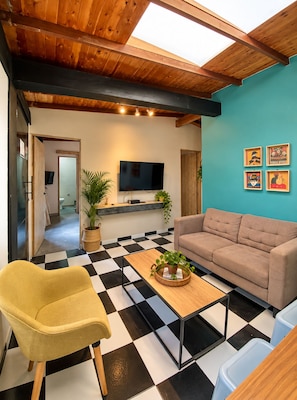 A modern living room with a checkered floor, a sofa, a yellow armchair, a coffee table with a plant, and a TV mounted on the wall. - New Listing (Medellín)