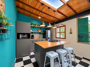 A kitchen with a wooden ceiling, a central island with stools, and a view through a window with a green door. - New Listing (Medellín)