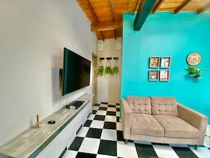 A living room with a black and white checkered floor, a beige sofa, a flat-screen TV on a wooden console, and a teal accent wall with framed pictures and a clock. - New Listing (Medellín)