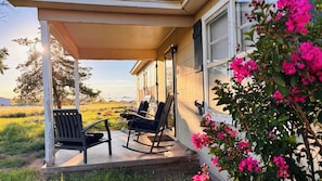 Eine überdachte Veranda mit zwei Schaukelstühlen und Blick auf ein Feld.