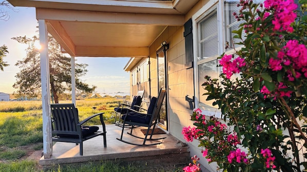 A covered porch with two rocking chairs and a view of a field.