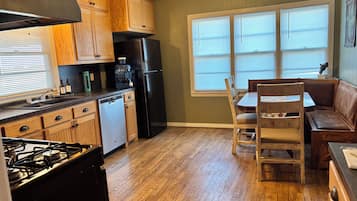 Una cocina con armarios de madera, un refrigerador negro, una cafetera y un comedor con sillas y un banco de madera.