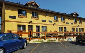 A multi-story building with a yellow facade, wooden balconies with flower boxes, and a parking area with cars. - Elizabeth Lake Lodge (Cranbrook)