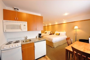 A compact hotel room with a kitchenette, a bed, a bedside table, and a lamp. - Elizabeth Lake Lodge (Cranbrook)