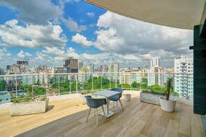 A balcony with a table and chairs, potted plants, and a city view. - {The~Urban~Escape}@Downtown Piantini+Gym+lounge (Santo Domingo)