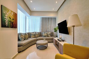 A modern living room with a sectional sofa, a round ottoman, a yellow armchair, a floor lamp, and a flat-screen TV mounted on the wall. - {The~Urban~Escape}@Downtown Piantini+Gym+lounge (Santo Domingo)