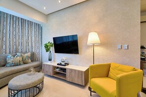 Ein modernes Wohnzimmer mit einer Couch, einem Hocker, einem gelben Sessel, einem Fernseher und einer Lampe.
